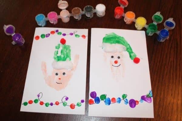 Elf Handprint craft - 2 Elf Handprint Christmas cards shown with a rainbow of colorful paint pots.