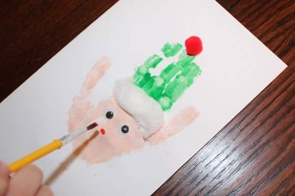 Child paints a nose on an elf handprint Christmas craft card