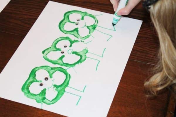 Child adding googly eyes and legs and arms to a preschool shamrock craft