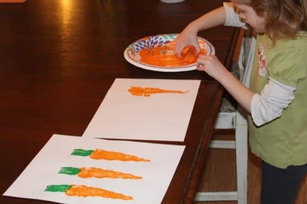 child making carrot stamps on a piece of paper with a completed project in the foreground