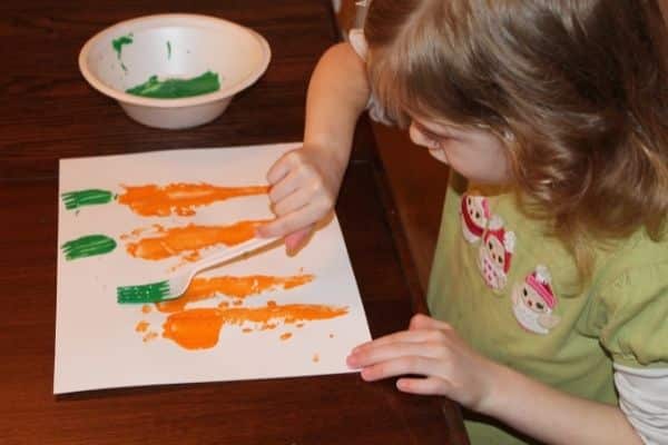 child using a fork and green paint to stamp carrot tops onto the carrot prints