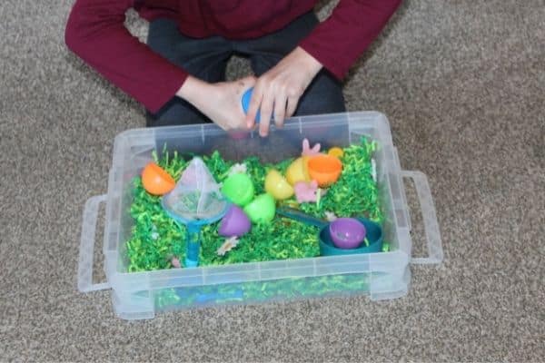 Child opening plastic Easter eggs in an Easter sensory bin