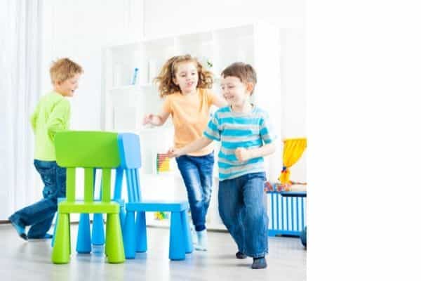 Several children walking around a group of chairs, playing musical chairs