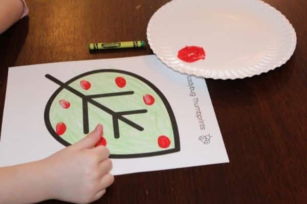Making thumbprint ladybugs - stamping thumb with red paint onto a green colored leaf template