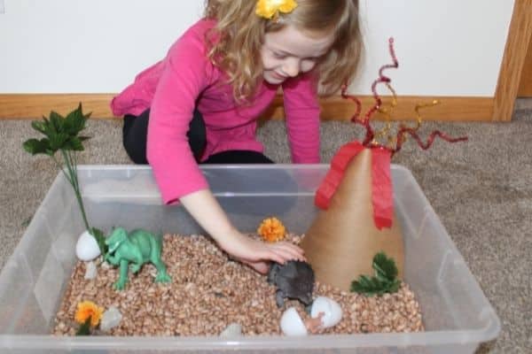 Girl playing with triceratops dinosaur toy in a sensory bin