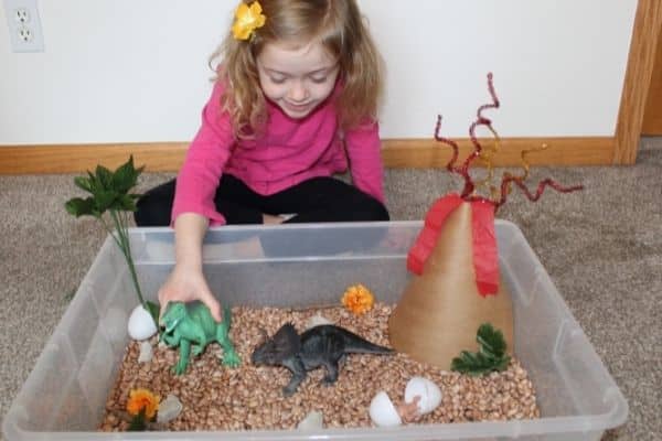 Girl playing with dinosaur sensory bin and pretend paper volcano