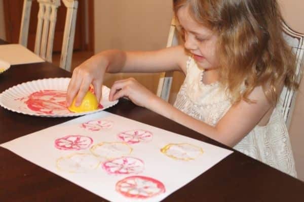 Child dipping half of a lemon into pink paint