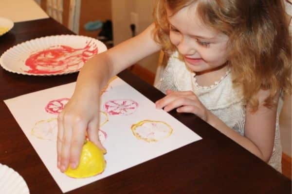 Child smiles as she adds pink lemon slice prints onto her page