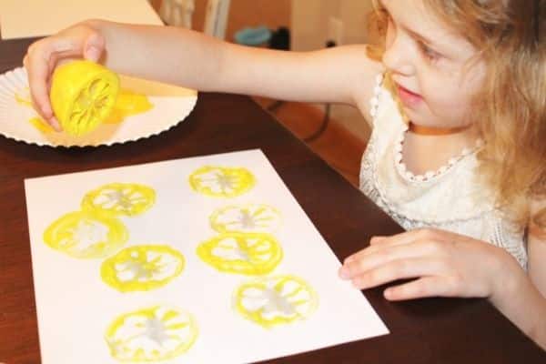 girl using a lemon to stamp yellow paint lemon slices onto a page