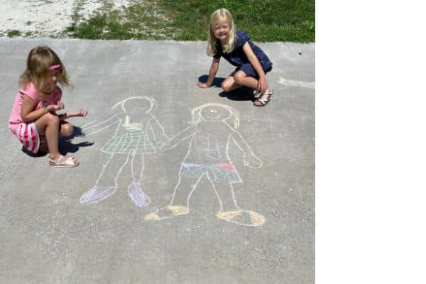 Children drawing themselves with sidewalk chalk outside.