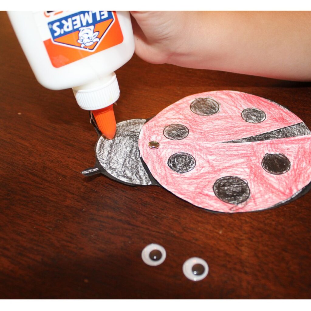 Child gluing on the eyes to the paper ladybug craft