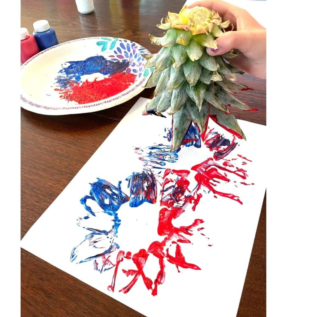 Pineapple Stamping Fireworks Craft for Preschool is a fun way to celebrate Independence Day!  Child stamping red and blue paint onto a page with a pineapple spike