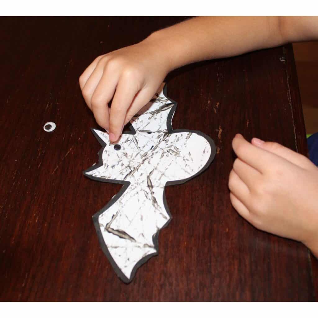 child pressing googly eyes onto the bat template craft