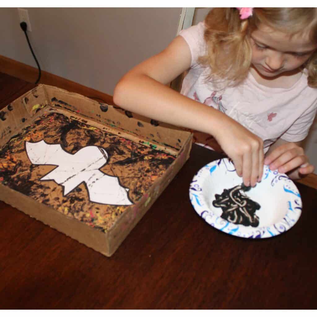 child dipping marble into black paint to marble paint a bat template