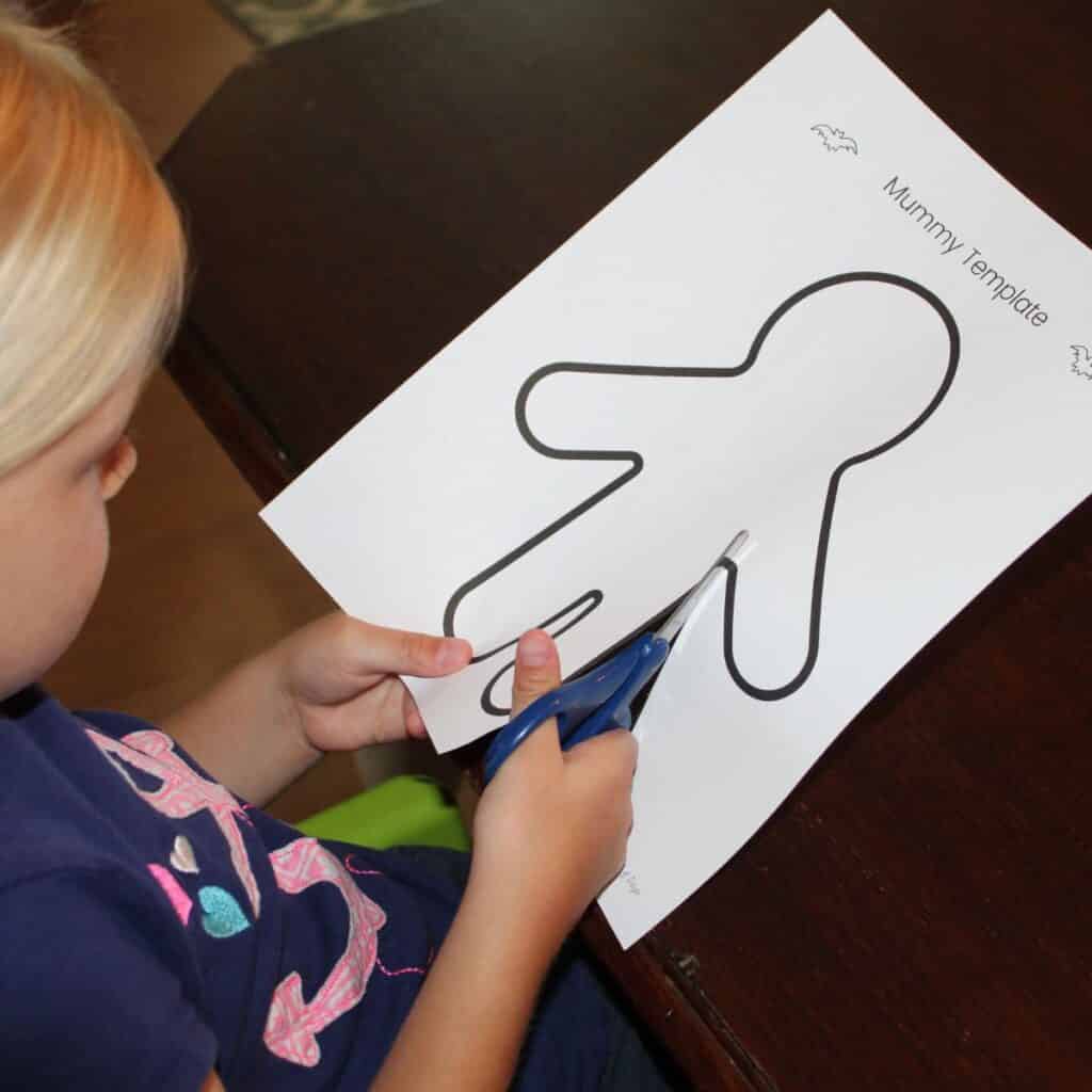 child cutting out the mummy template for the easy preschool mummy craft