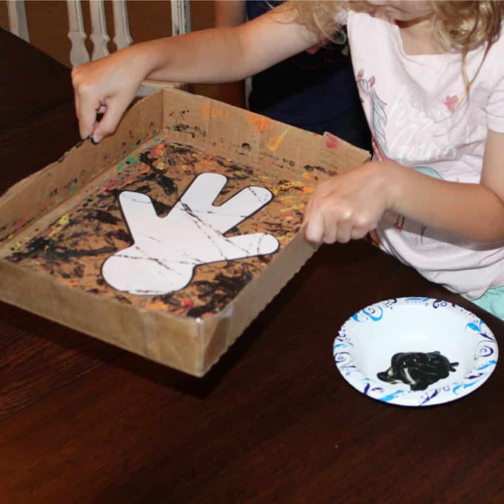 Child holding a shallow box with the mummy template inside, marble painting the mummy 