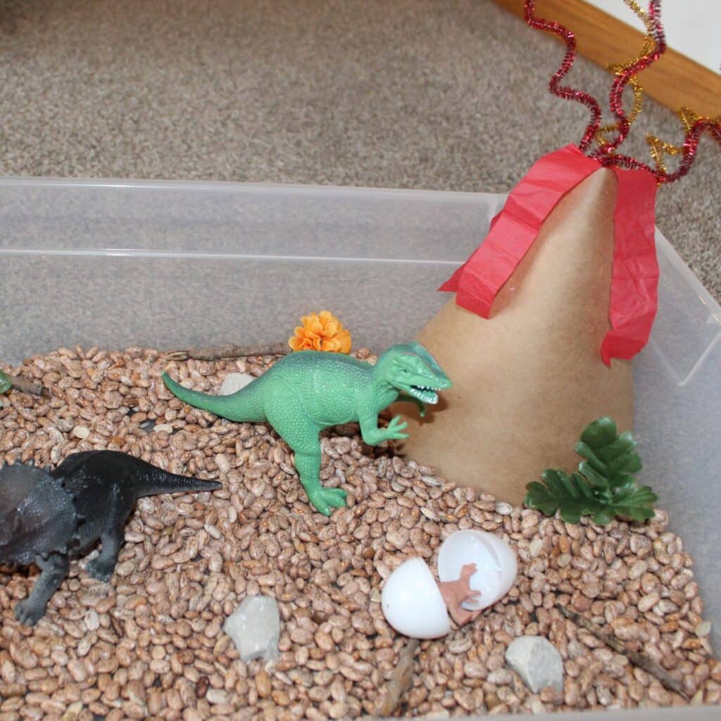 Dinosaur Sensory Bin from Simply Full of Delight featuring baby dinos hatching from eggs, beans rocks, and large dinos.