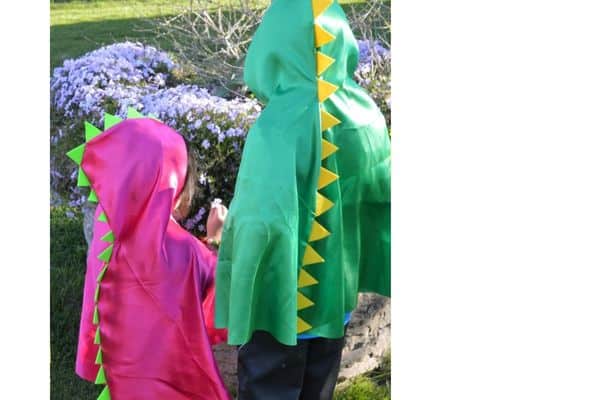 Dinosaur Capes by Capes and More on etsy - shown green cape with yellow spikes and a pink cape with green dino spikes