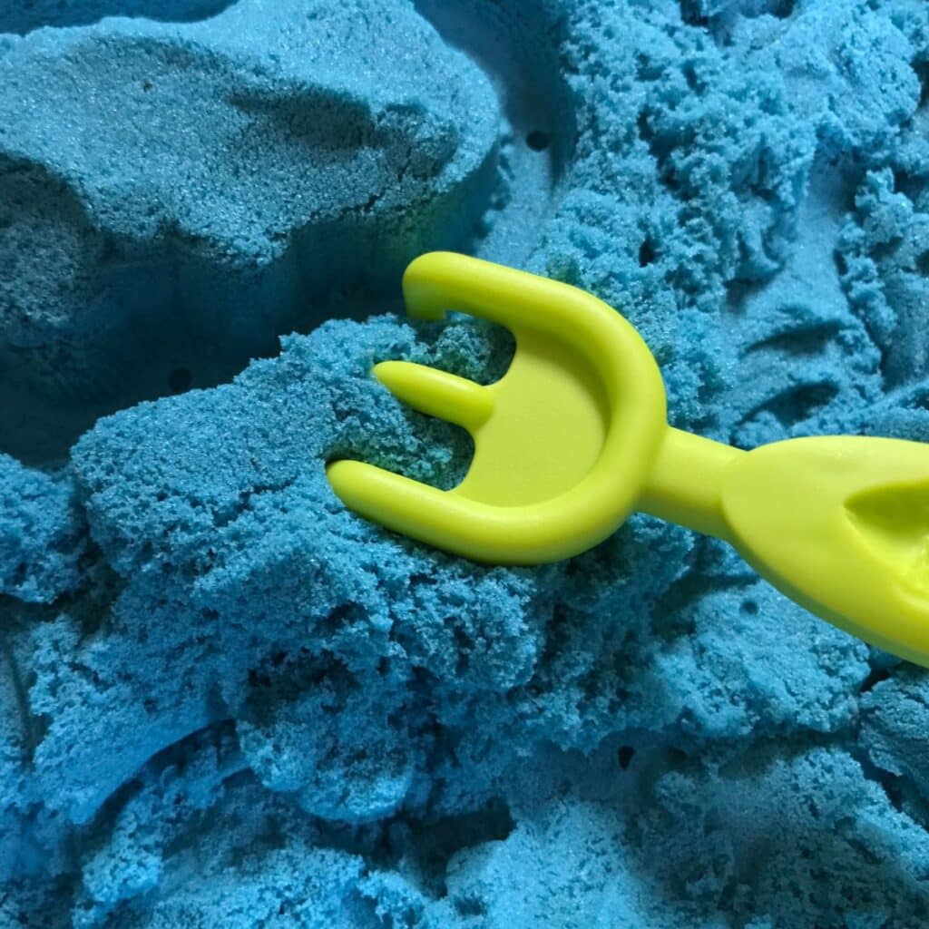 blue kinetic sand shown with a toy rake tool