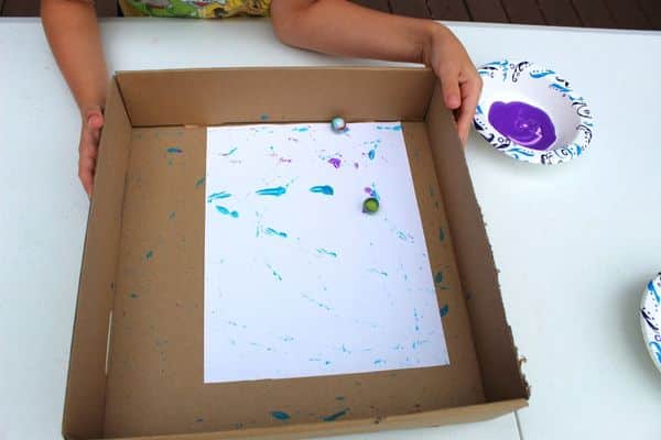 Child using 2 balls to paint a page - marble painting - painting with balls activity