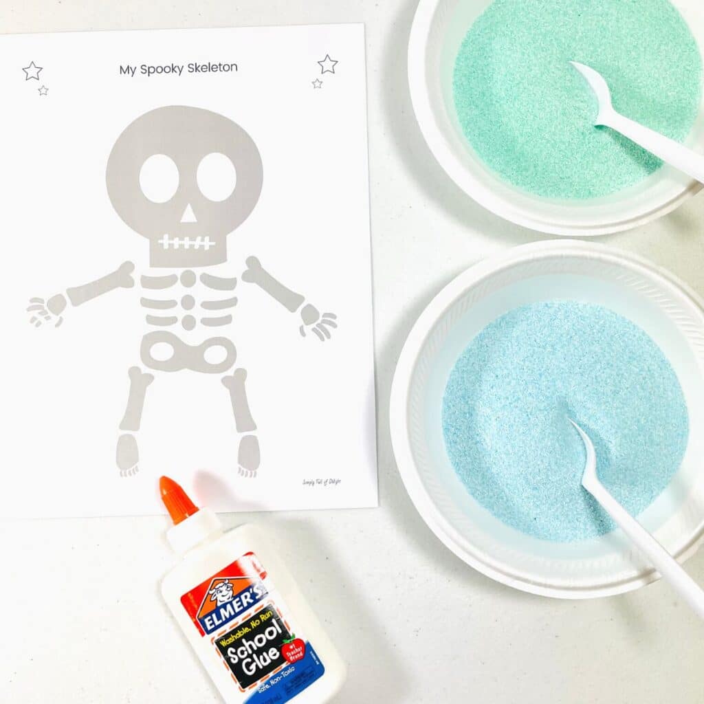 Supplies for easy skeleton craft for preschool - 3 colors of sand, elmer's glue and a skeleton template (free printable)