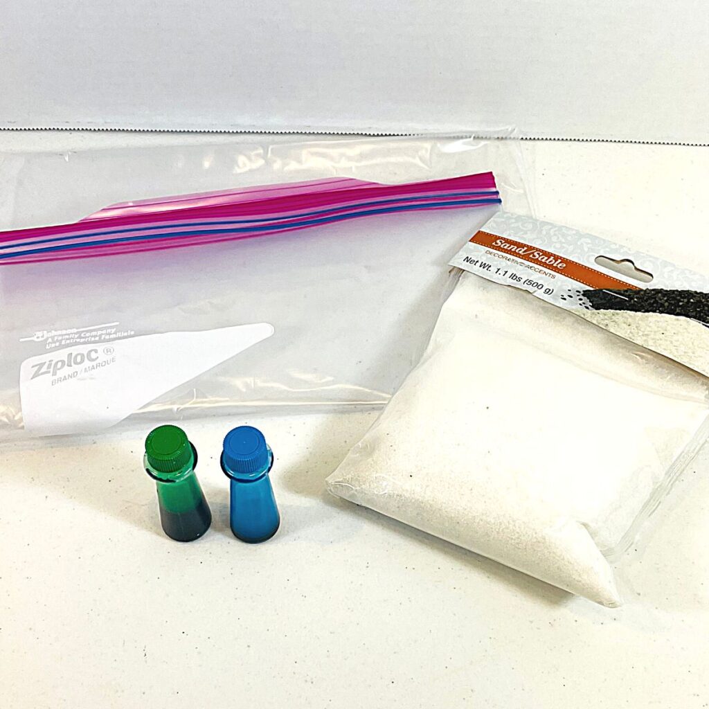supplies for colored sand including gallon size plastic bag, sand, and food coloring