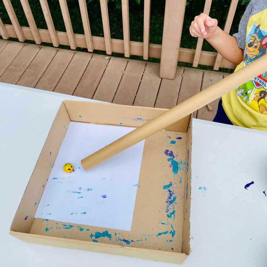 painting with balls - preschool child shown using a cardboard tube to send a ball onto a page to paint