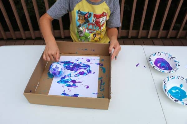 wiffle ball painting - child shown using purple and blue paint to create artwork with a wiffle ball 