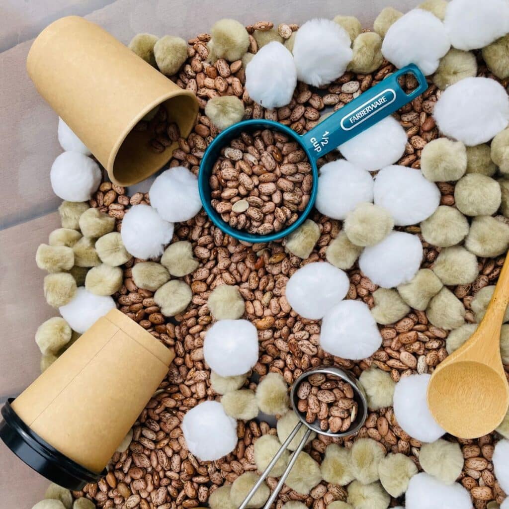 Hot Chocolate Sensory Bin for Preschoolers.  This Pom Pom Sensory Bin contains beans, pom poms, coffee cups, scoops and more!  Such a fun hot cocoa sensory play idea!