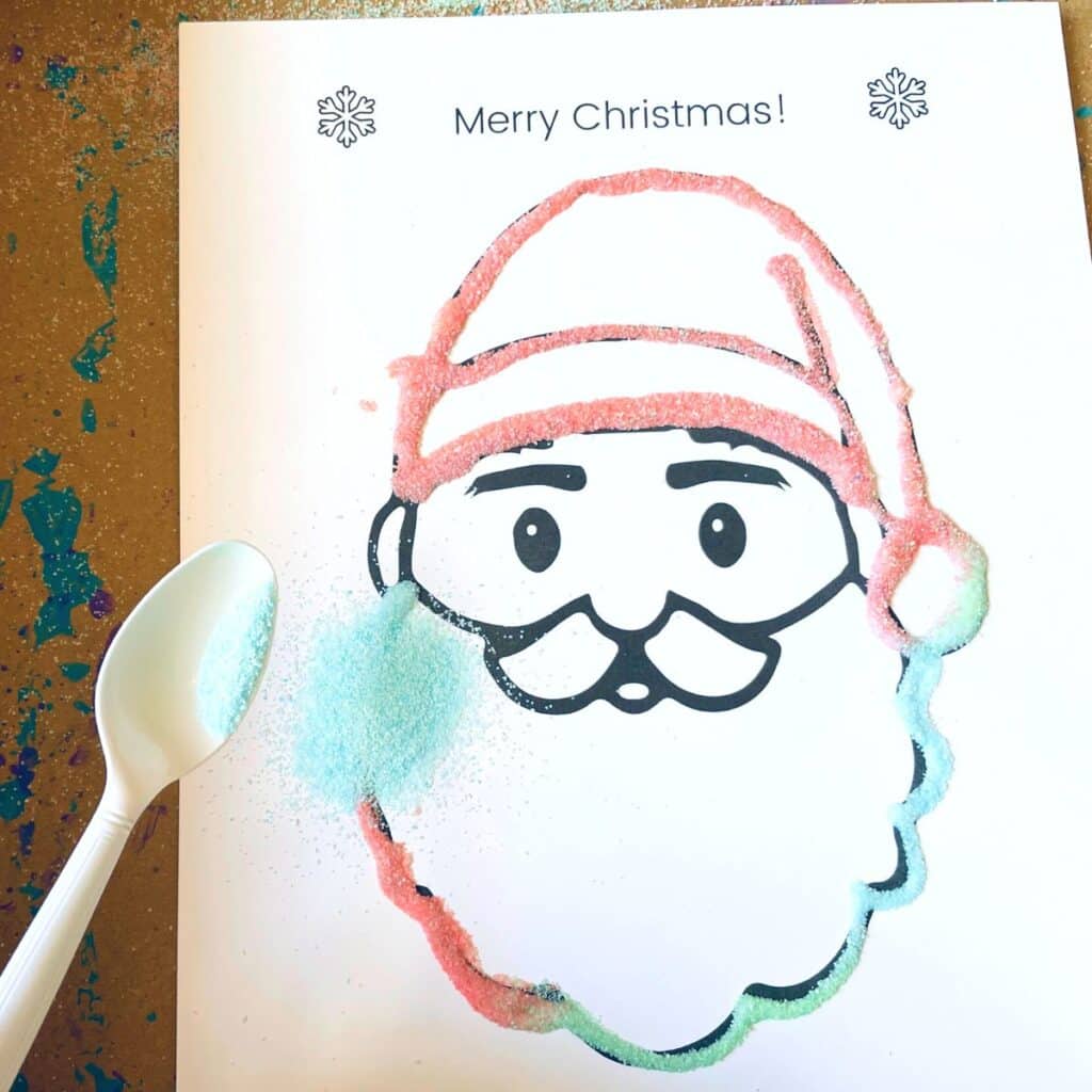 Santa face printable with colored sand being applied with glue for an easy preschool Santa craft