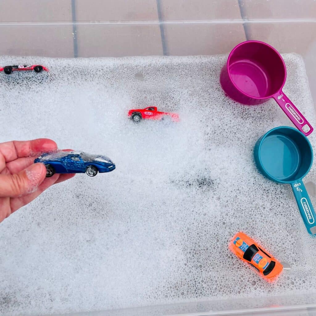 Car Wash Sensory Bin - a fun play car wash for kids - this car sensory play idea is perfect for a transportation unit - shown:  tub of water with bubbles, toy cars, and scoops