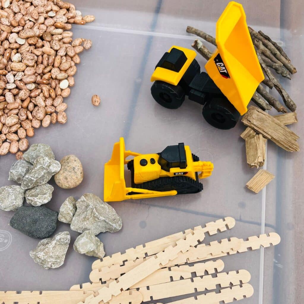 construction sensory bin - a construction themed sensory activity - contains construction vehicles, beans, rocks, sticks, and wood chips