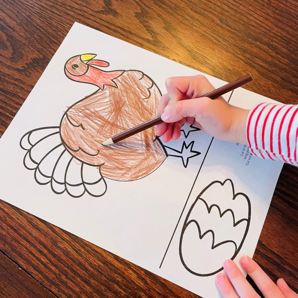child coloring a paper turkey craft with a brown colored pencil