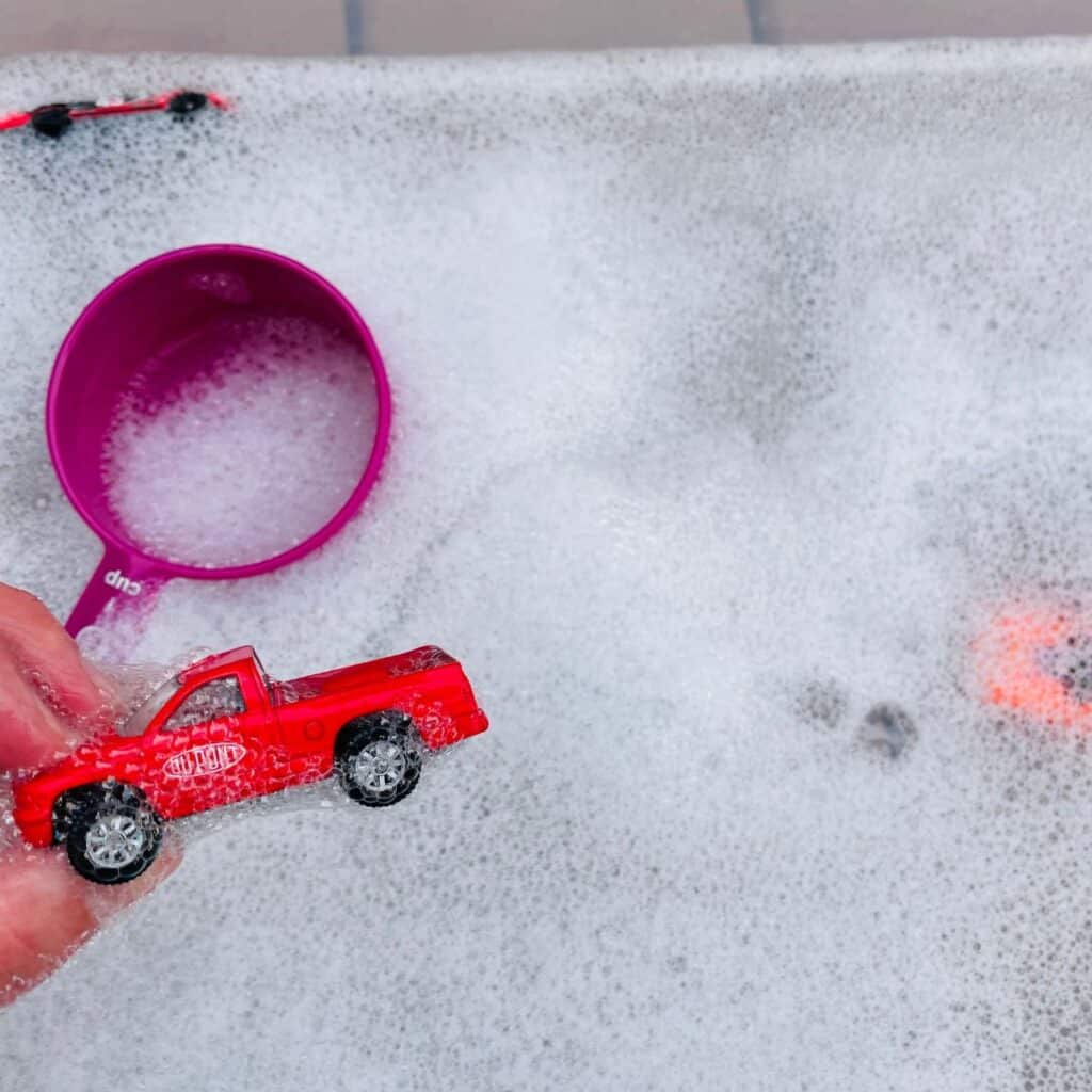 Car wash sensory bin for preschoolers - shown: toy truck with background of tub of bubbly water