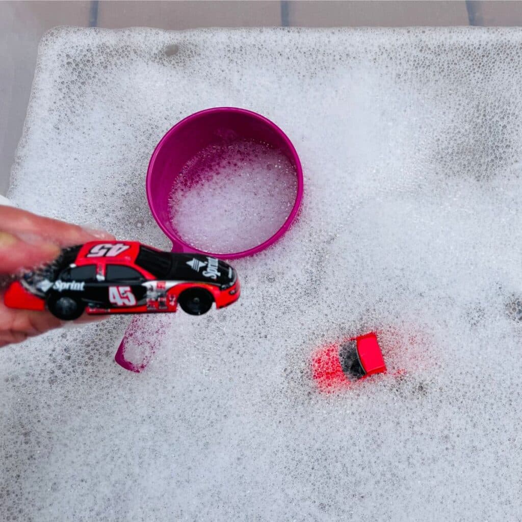 car wash sensory bin - person holding car above soapy water in a plastic container