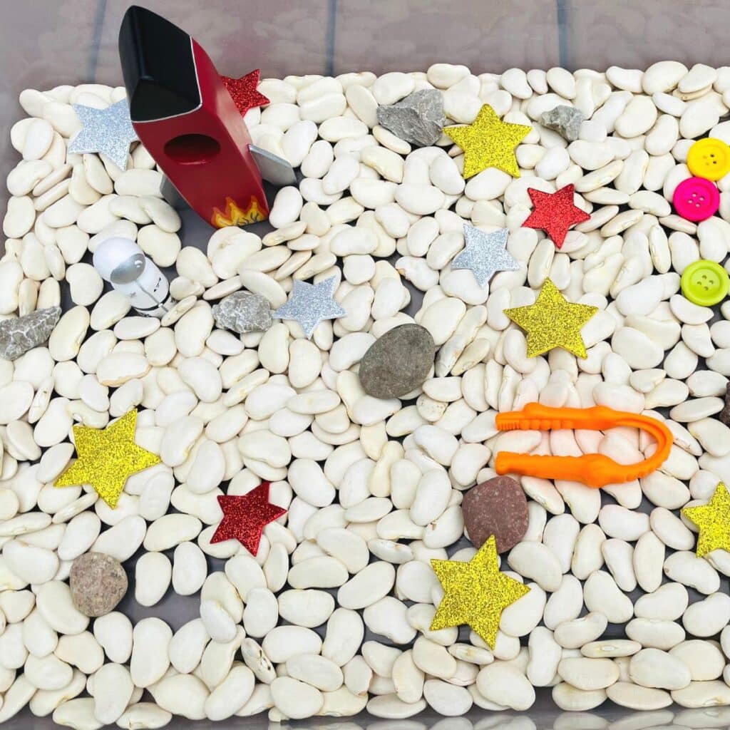 space sensory bin - a fun space sensory play idea including lima beans, buttons, foam stars, rocks, tweezers, wooden rockets