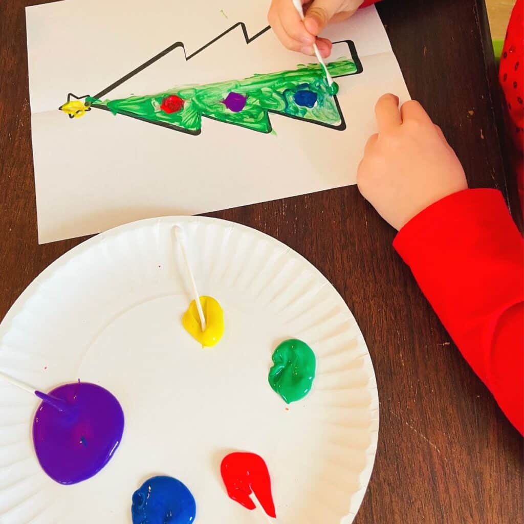 child painting a symmetry Christmas tree craft for kids - a free printable Christmas tree template is painted on the line of symmetry, then folded over to create a symmetrical print