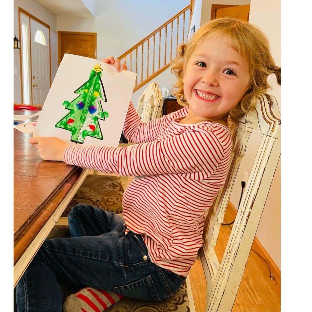 Child holding symmetry Christmas tree craft and smiling