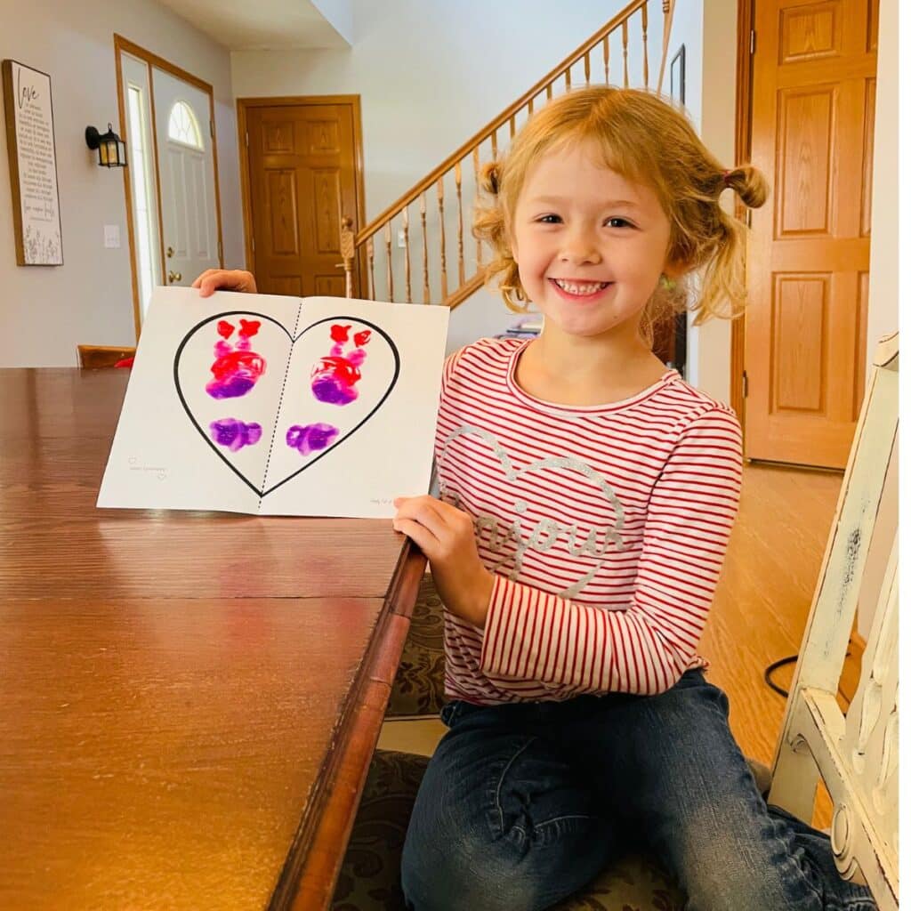 child displaying a symmetry heart craft for Valentine's Day