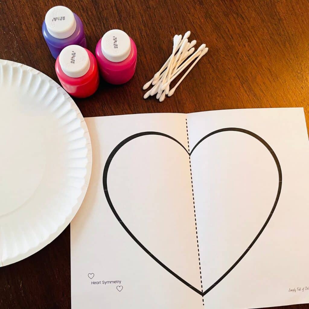 supplies for symmetry heart craft for Valentine's Day including the free heart template, paper plate, paint and q-tips