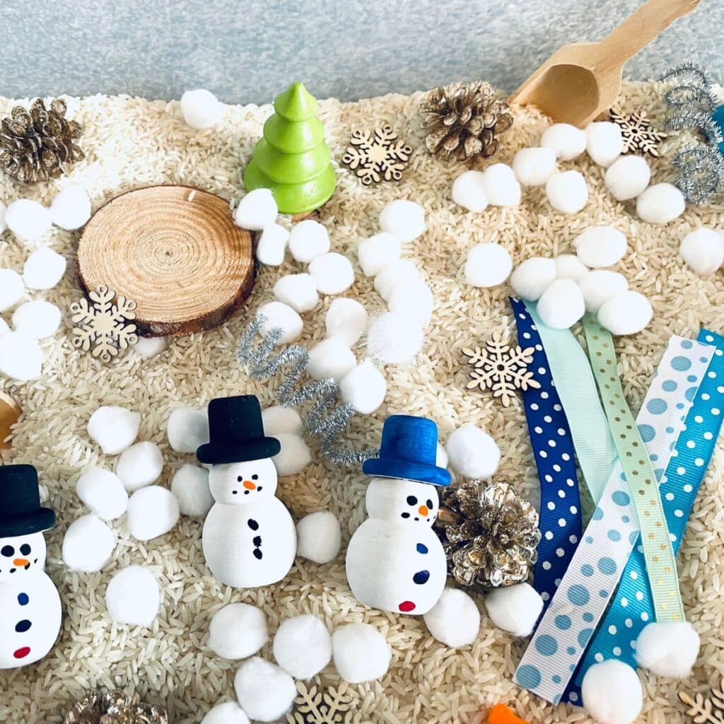 snowman winter sensory bin - a winter sensory table idea - rice, pom poms, snowmen, wooden snowflakes, and more