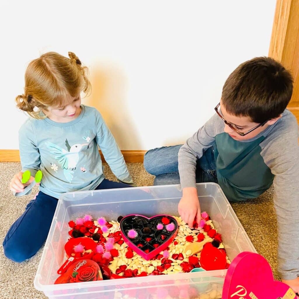 children playing with the valentines' day sensory bin - a chocolate box sensory bin for valentines day