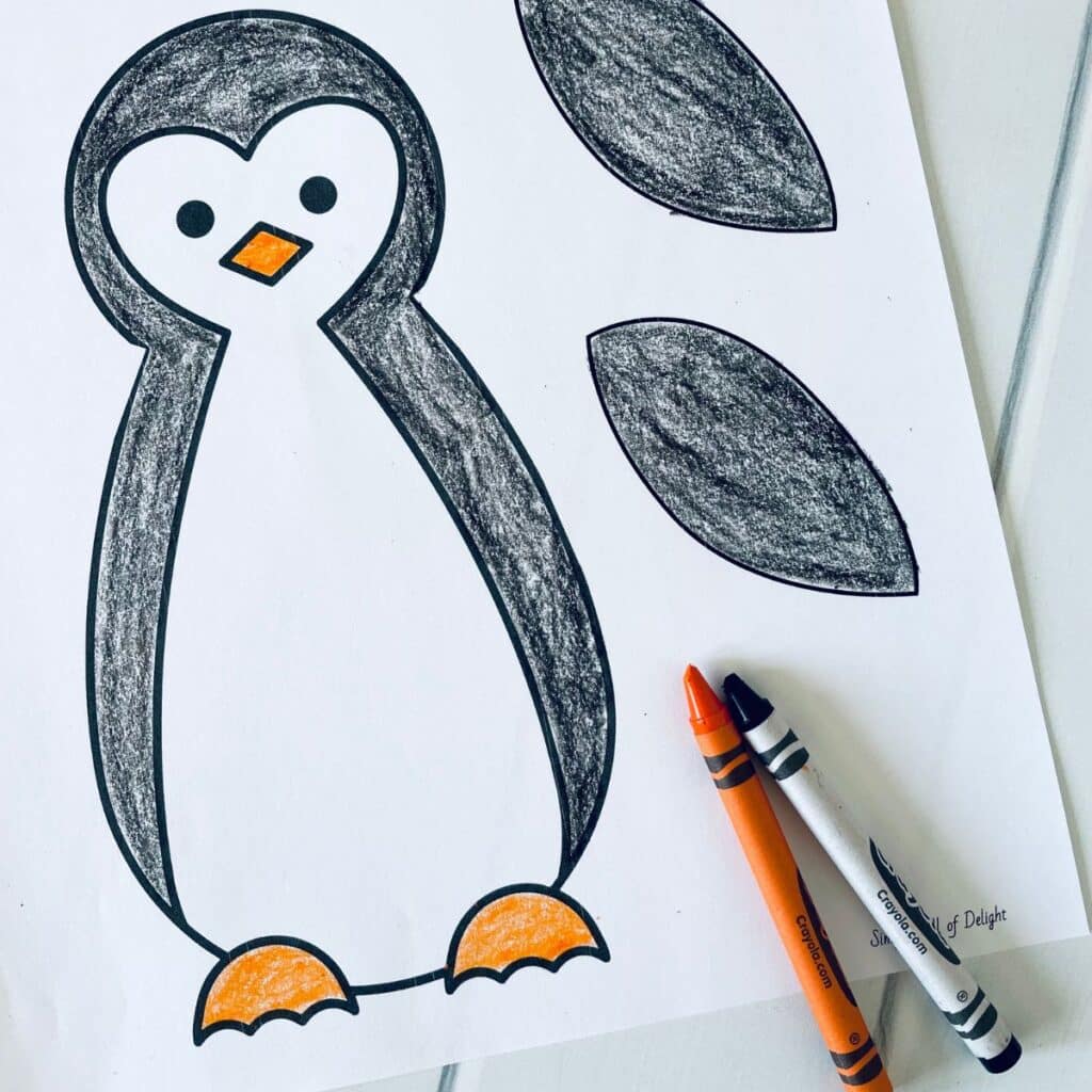 paper penguin craft colored with a black crayon and orange crayon