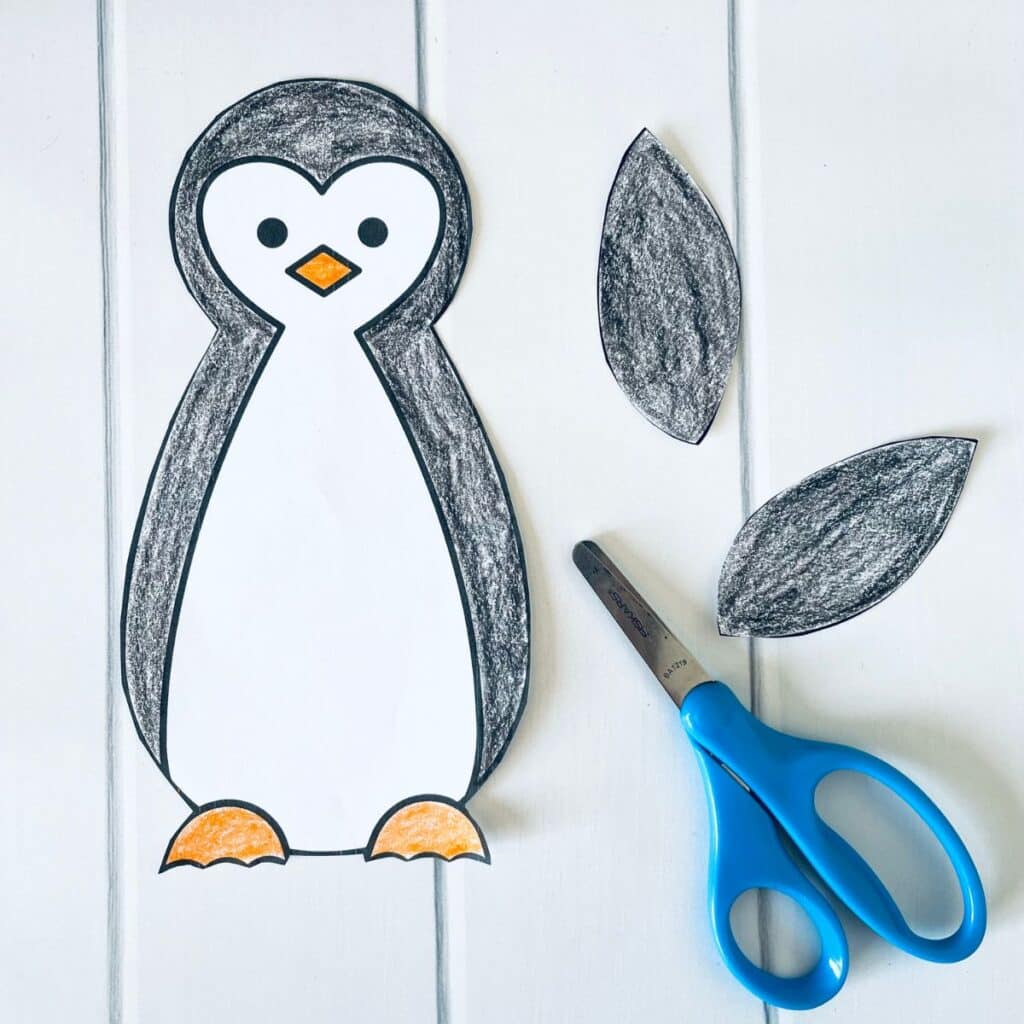 paper penguin template pieces are cut out with scissors.