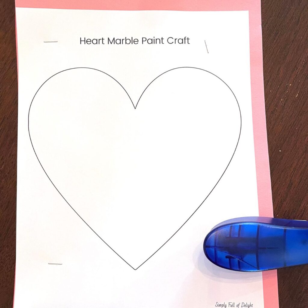 Heart marble paint craft template being stapled to colored paper pile
