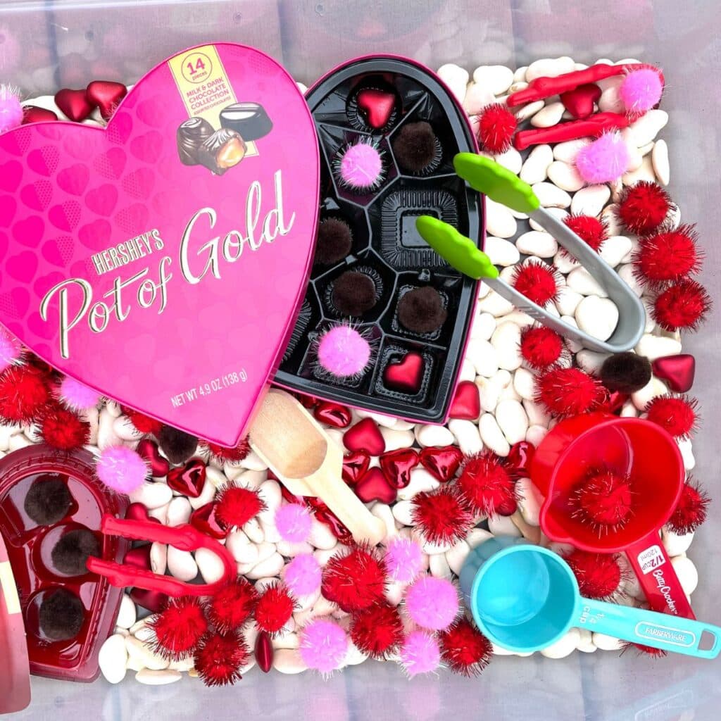 valentine's day sensory bin with pom poms, tongs, chocolate box, beans and more!