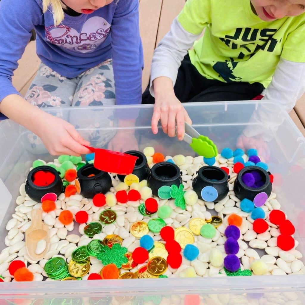 girls playing with tongs adding pom poms to the correct color bucket