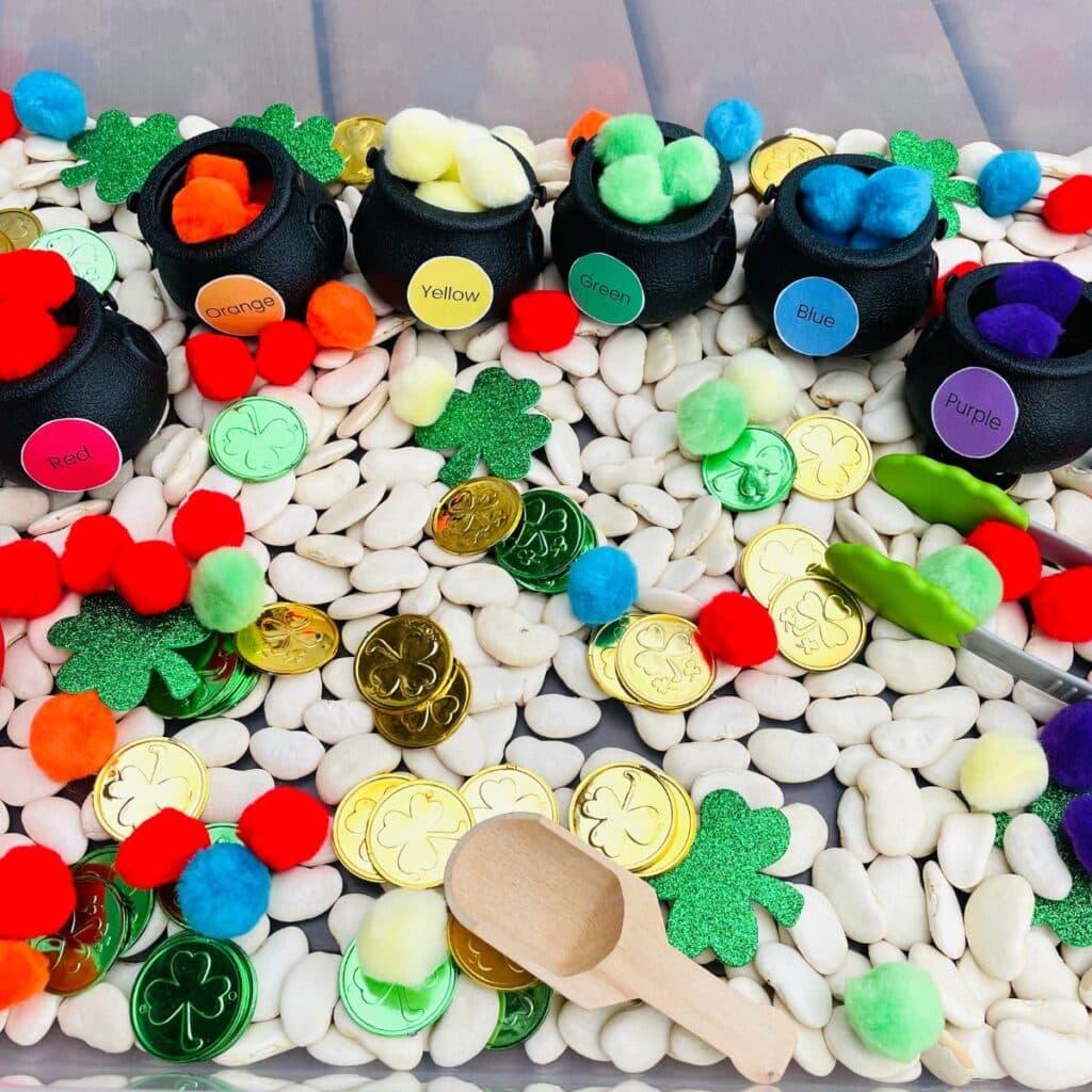 saint patricks day sensory bin with rainbow pom poms, pots and tongs
