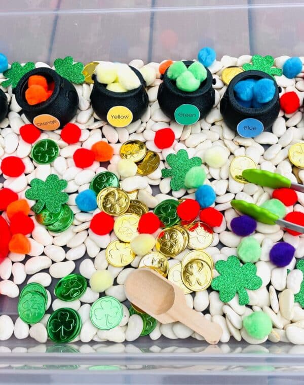 St. Patrick's day sensory bin filled with rainbow colored pom poms, gold coins, and pots of gold.
