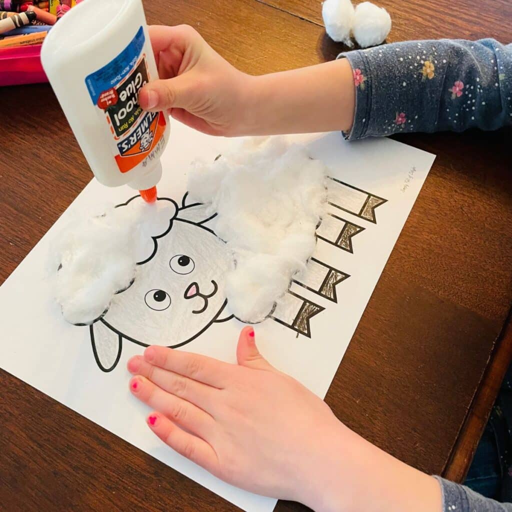 child adding glue and cotton balls to a sheep craft for preschool